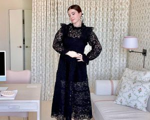 Nell Diamond wears a black frilly dress in her office with patterned wallpaper