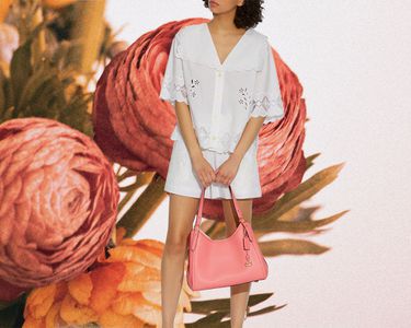 Woman carrying Coach purse against a floral background.