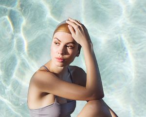 A woman in a swim cap and bathing suit, hand on her head