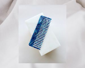A beautiful blue wide-tooth comb on a white background.