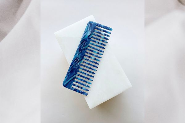 A beautiful blue wide-tooth comb on a white background.