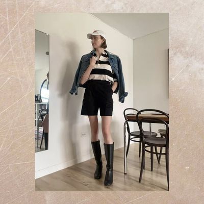 Byrdie writer wears tailored shorts with boots, striped shirt, denim jacket, and cap