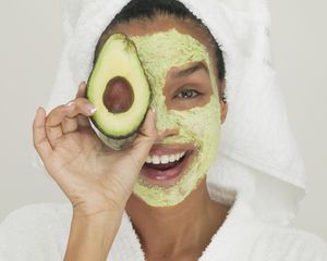 Portrait of a young woman wearing a facial mask holding a slice of avocado