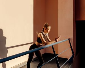 Woman in workout gear standing on a balcony, looking at her phone