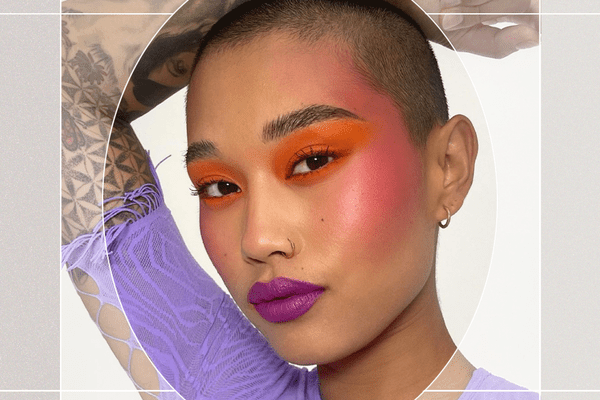 Portrait of AAPI Subject with Buzzcut Wearing Bold Orange Eyeshadow that Blends into Pink Blush Draping and Purple Lipstick