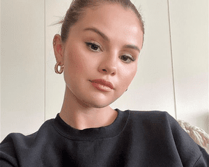 Selena Gomez wearing gold hoops and black sweatshirt