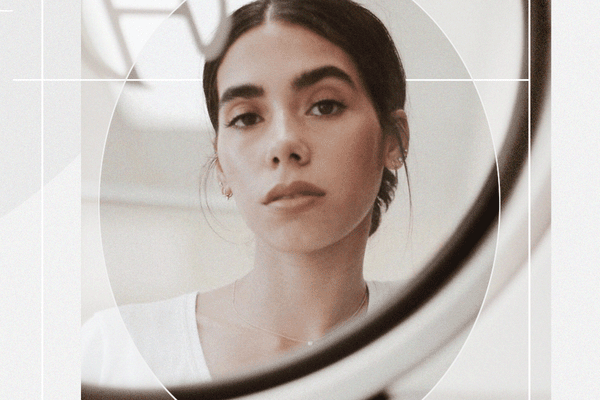 Portrait of a Woman Looking at Her Reflection in a Mirror with Minimal, Classic Makeup in a Loose Low Bun 